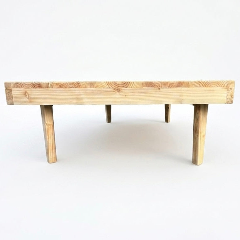 A minimalist wooden low table or bench with a thick rectangular plank top and four tapered legs, shown against a plain white background.